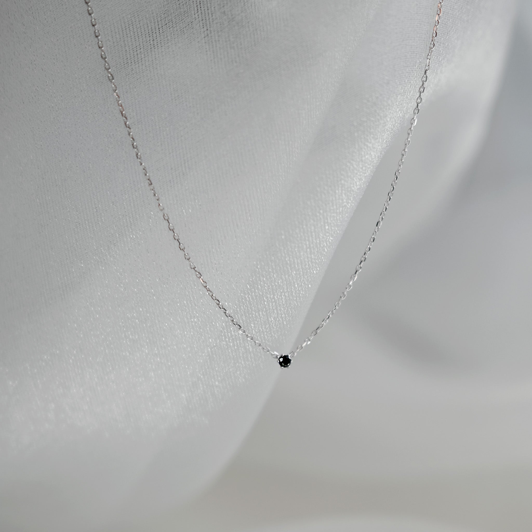 Delicate silver necklace with a small black pendant on a light gray background