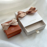Two jewelry boxes with ribbons, one white and one brown, on a light background.
