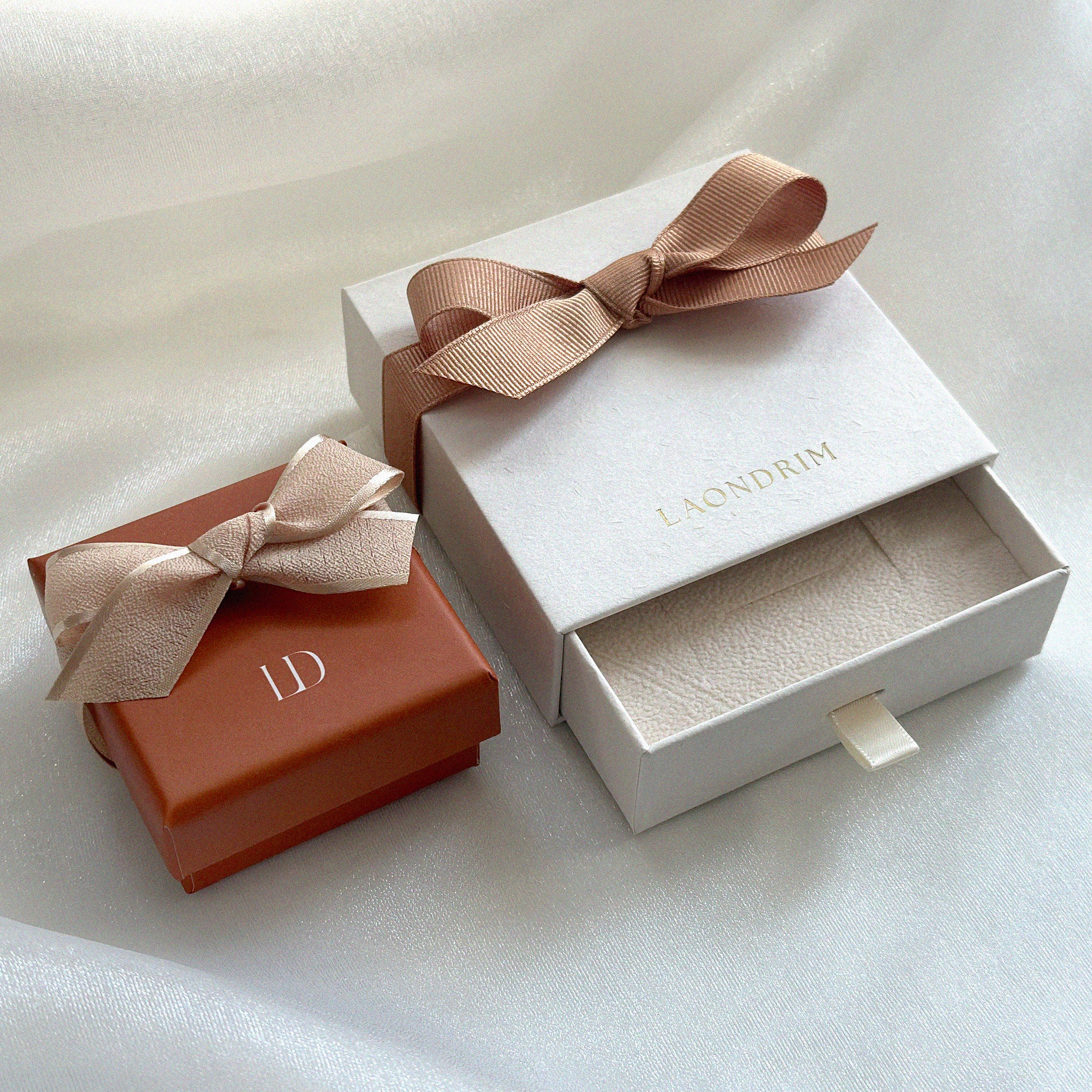 Two jewelry boxes with ribbons, one white and one brown, on a light background.