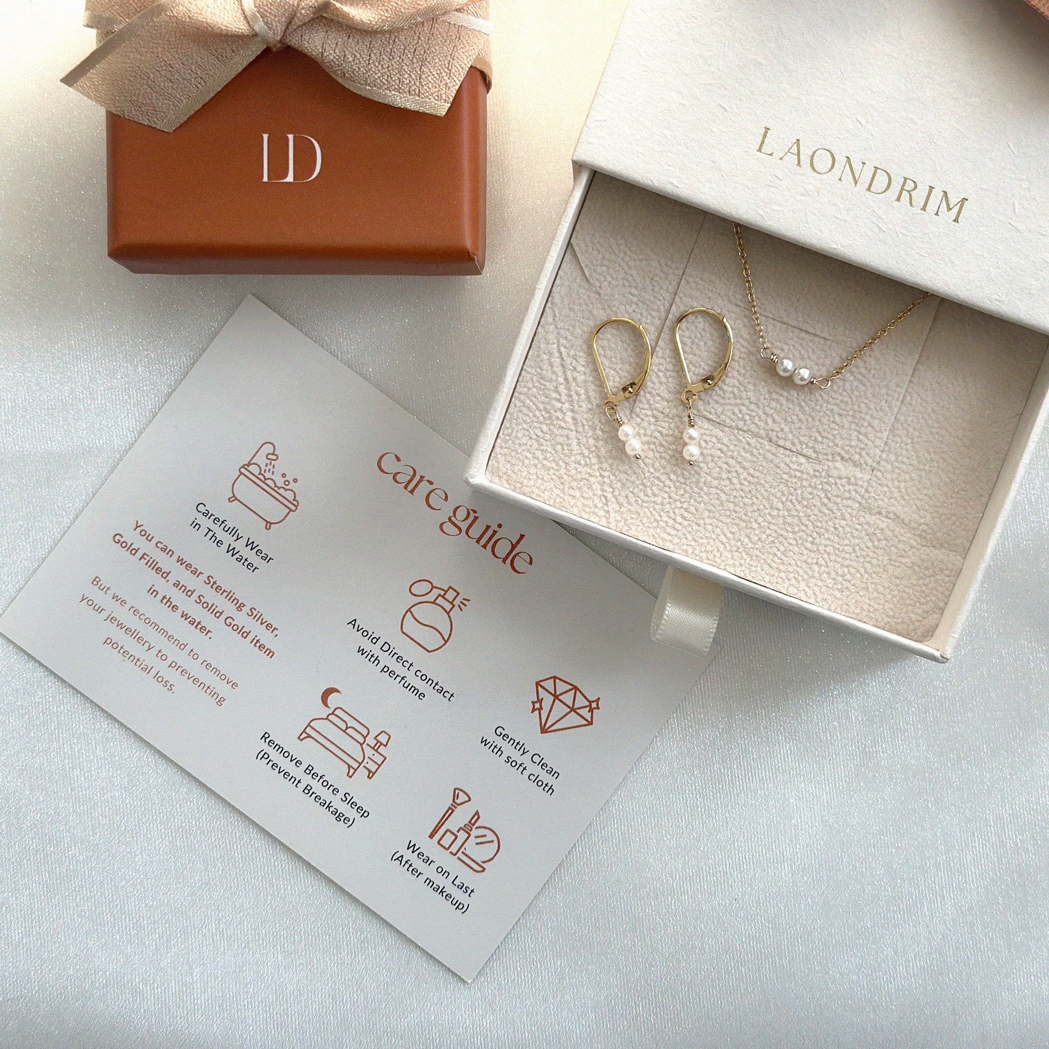 Jewelry set with earrings and a necklace in an open box, accompanied by a care guide and branded card.