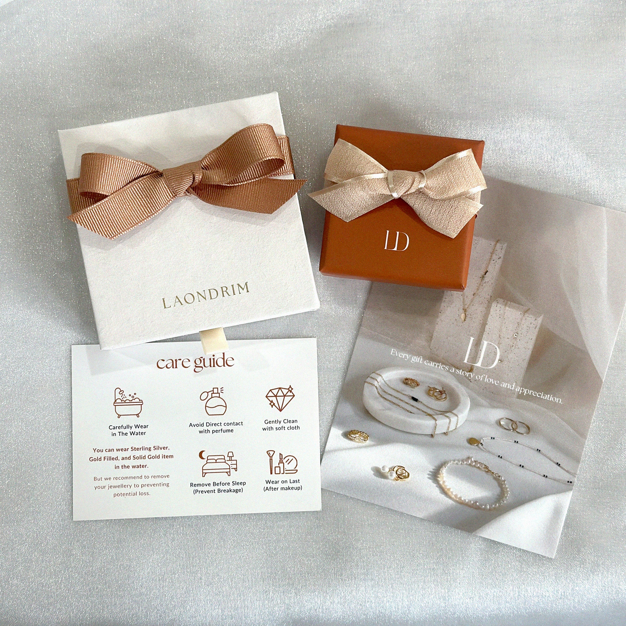 Jewelry set with branded box, care guide, and product images on a light gray background