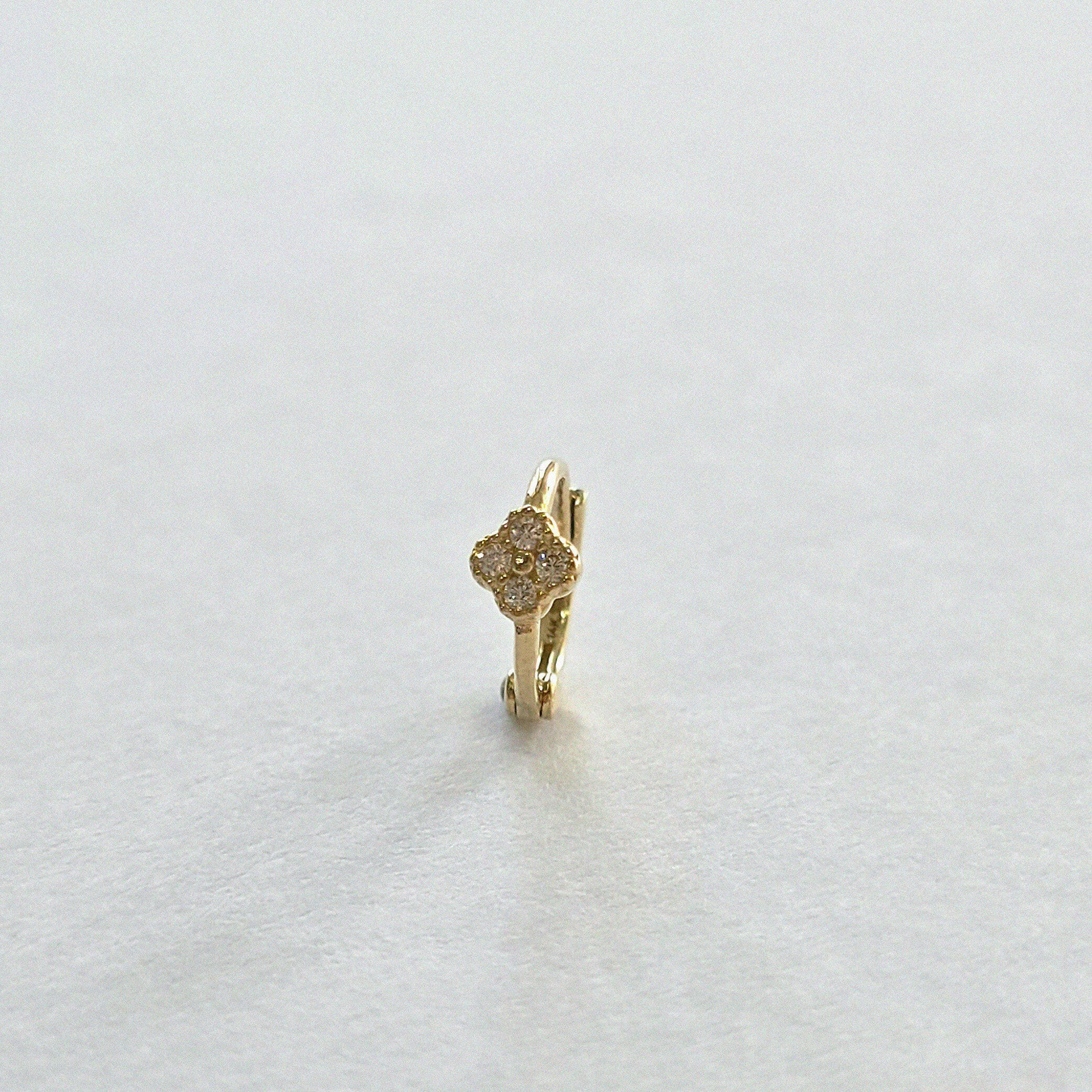 Front-facing view of huggie hoop earring with cubic zirconia clover accent