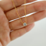 Gold necklace with a diamond pendant held between fingers on a blurred background