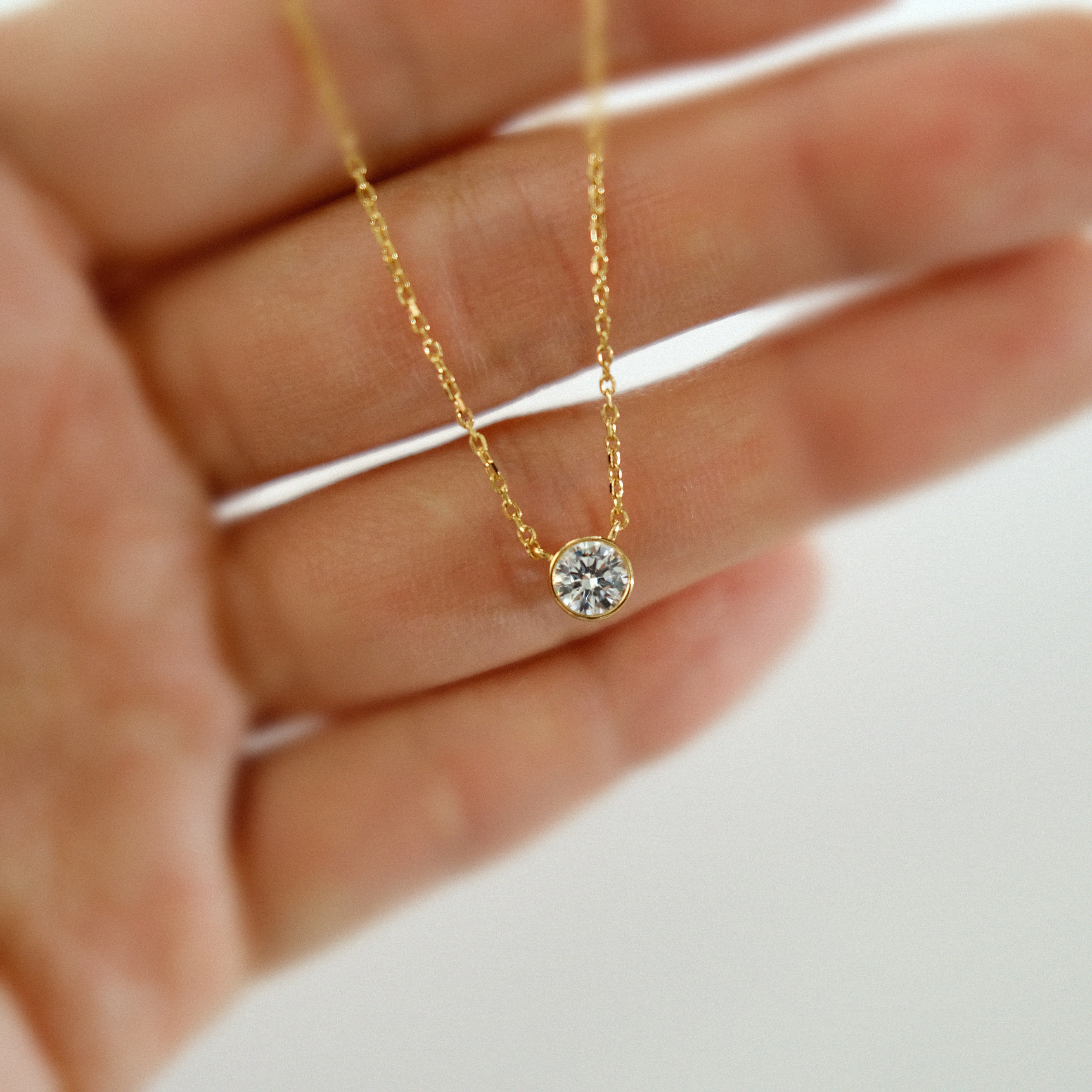 Gold necklace with a diamond pendant held between fingers on a blurred background