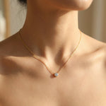 Gold necklace with a small pendant on a person's neck against a neutral background