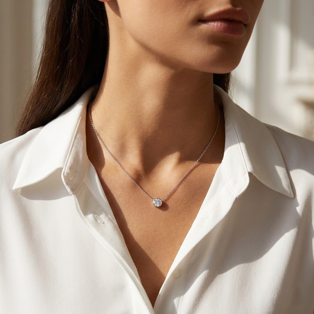 Woman wearing a white shirt with a delicate necklace featuring a round pendant.
