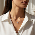 Woman wearing a white shirt with a delicate necklace featuring a round pendant.