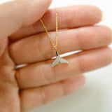 Gold necklace with a whale tail pendant held in a hand against a neutral background