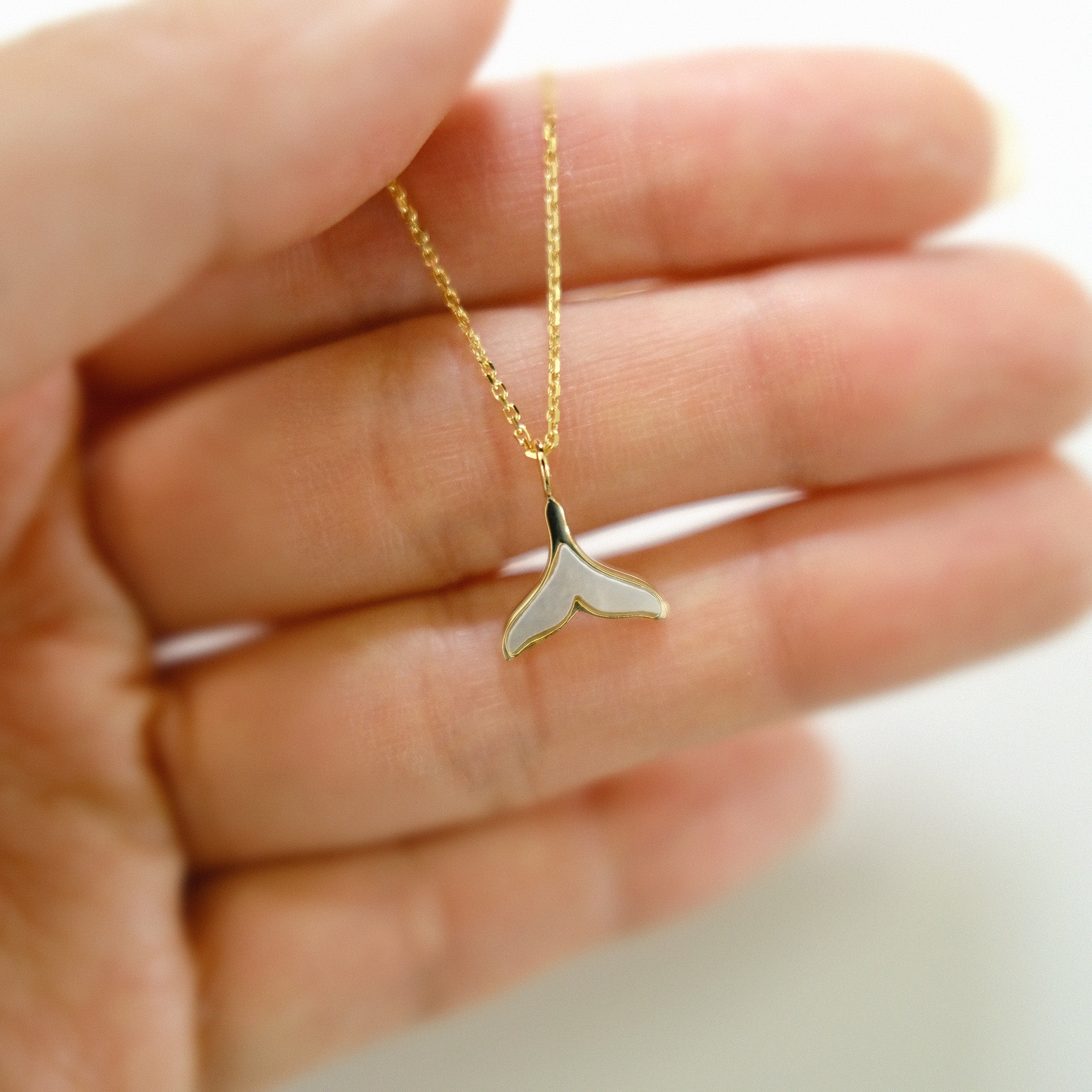 Gold necklace with a whale tail pendant held in a hand against a neutral background