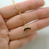 Gold whale tail necklace on a hand with a blurred background