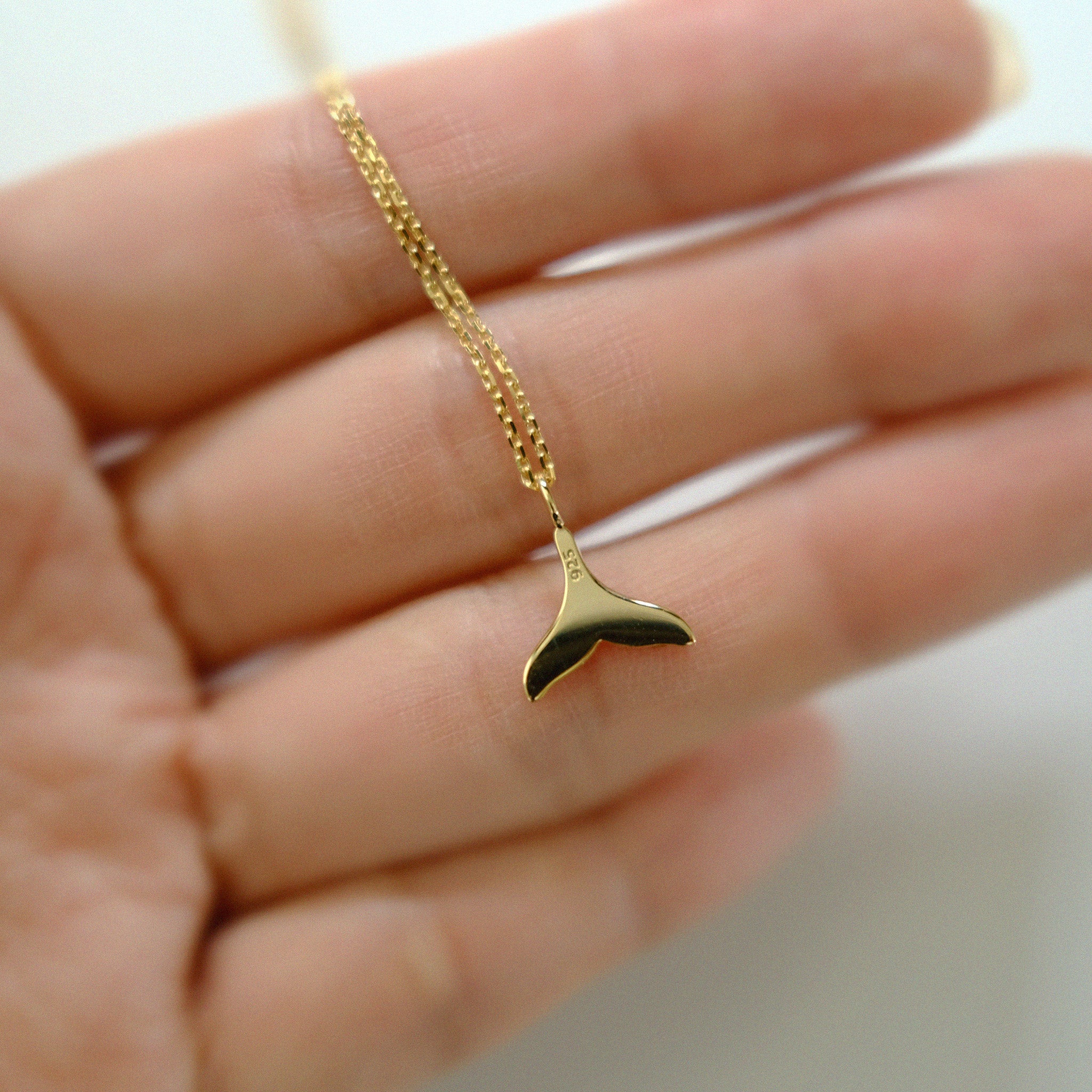 Gold whale tail necklace on a hand with a blurred background