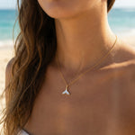 Woman wearing a gold necklace with a whale tail pendant on a beach.