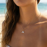 Woman wearing a gold necklace with a whale tail pendant on a beach.