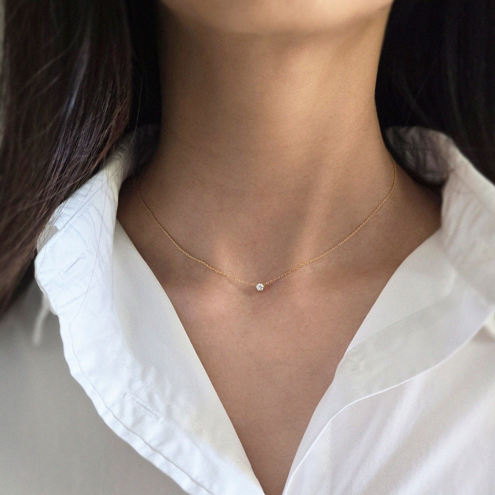 Person wearing a delicate gold necklace with a small pendant on a plain background