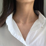 Person wearing a delicate gold necklace with a small cubic zirconia pendant on a plain background