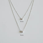 Silver necklace with two different chain widths on a light gray background