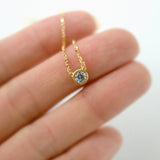 Gold necklace with a diamond pendant held between fingers on a blurred background