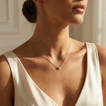 Woman wearing a delicate necklace with a small pendant against a neutral background