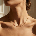 Close-up of a person wearing a gold necklace with a neutral background