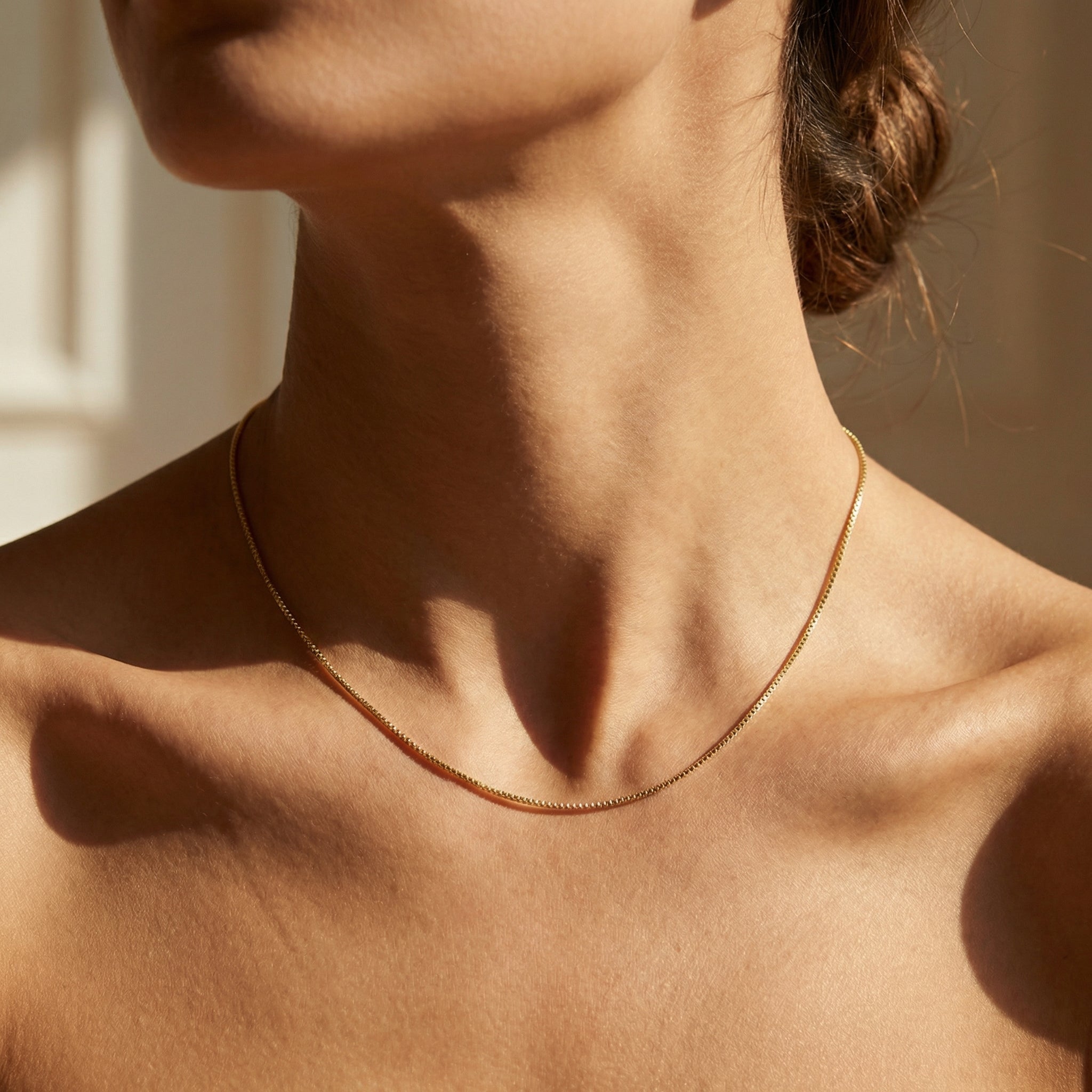 Close-up of a person wearing a gold necklace with a neutral background