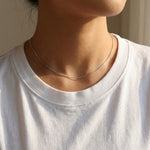 Person wearing a delicate silver necklace with a plain background