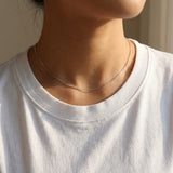 Person wearing a delicate silver necklace with a plain background