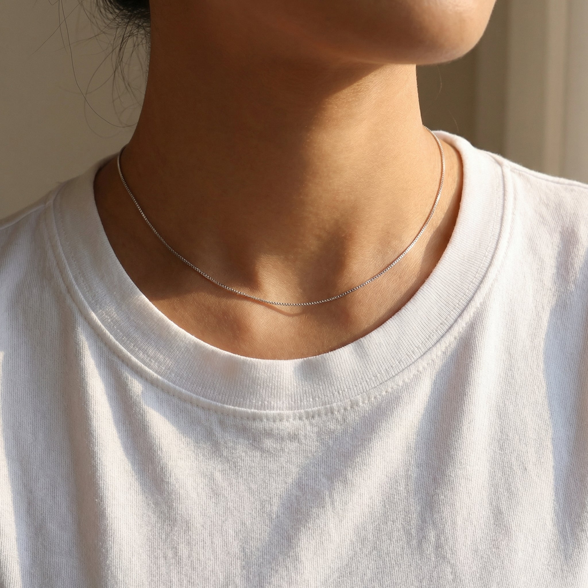 Person wearing a delicate silver necklace with a plain background