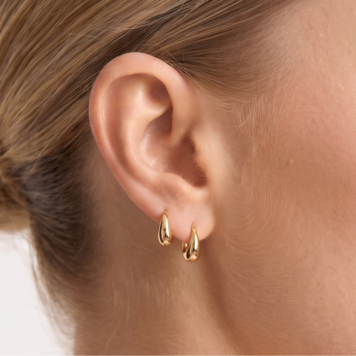 Close-up of a woman wearing gold hoop earrings with a plain background