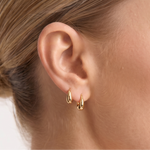 Close-up of a woman wearing gold hoop earrings with a plain background