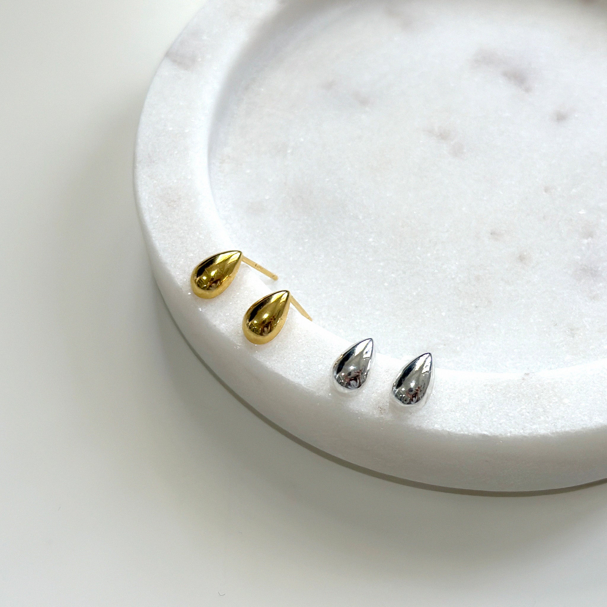 Gold and silver earrings on a white marble surface