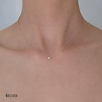 Gold necklace with a small pendant on a person's neck, displayed against a neutral background.