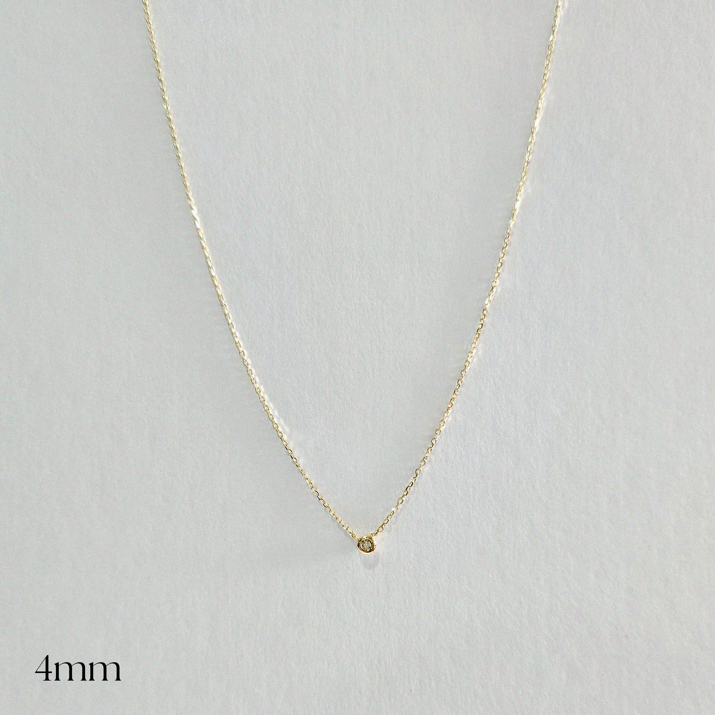 Gold necklace with a small round pendant on a light gray background