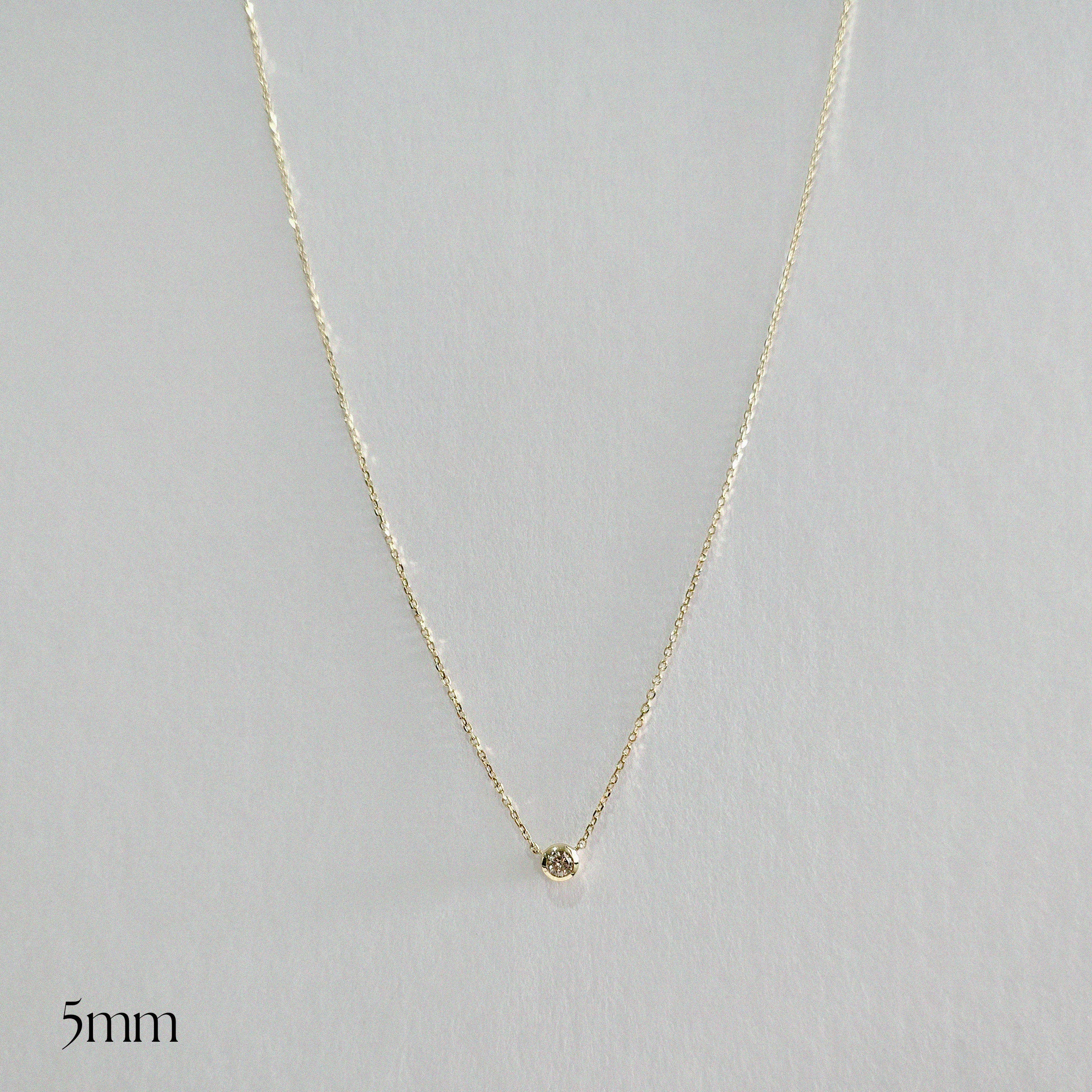 Gold necklace with a small round pendant on a light gray background
