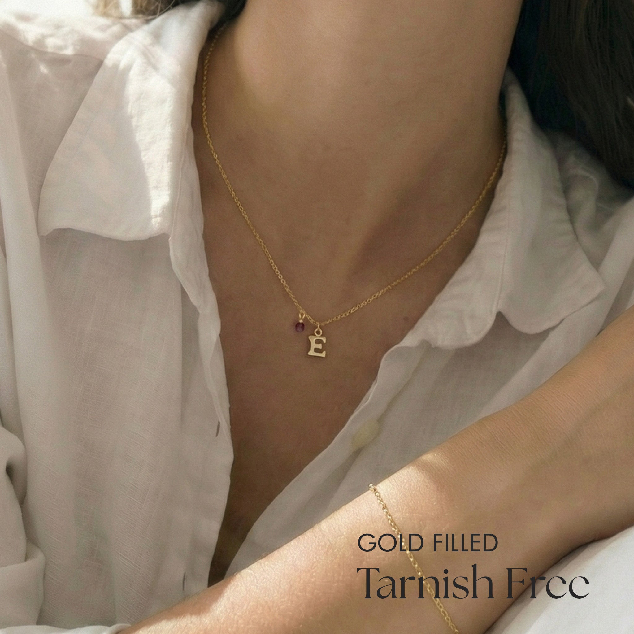 Gold filled necklace with letter 'E' pendant worn by a person, against a neutral background.