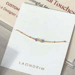 Gold bracelet with multicolored beads on a white card with 'LAONDRIM' branding.