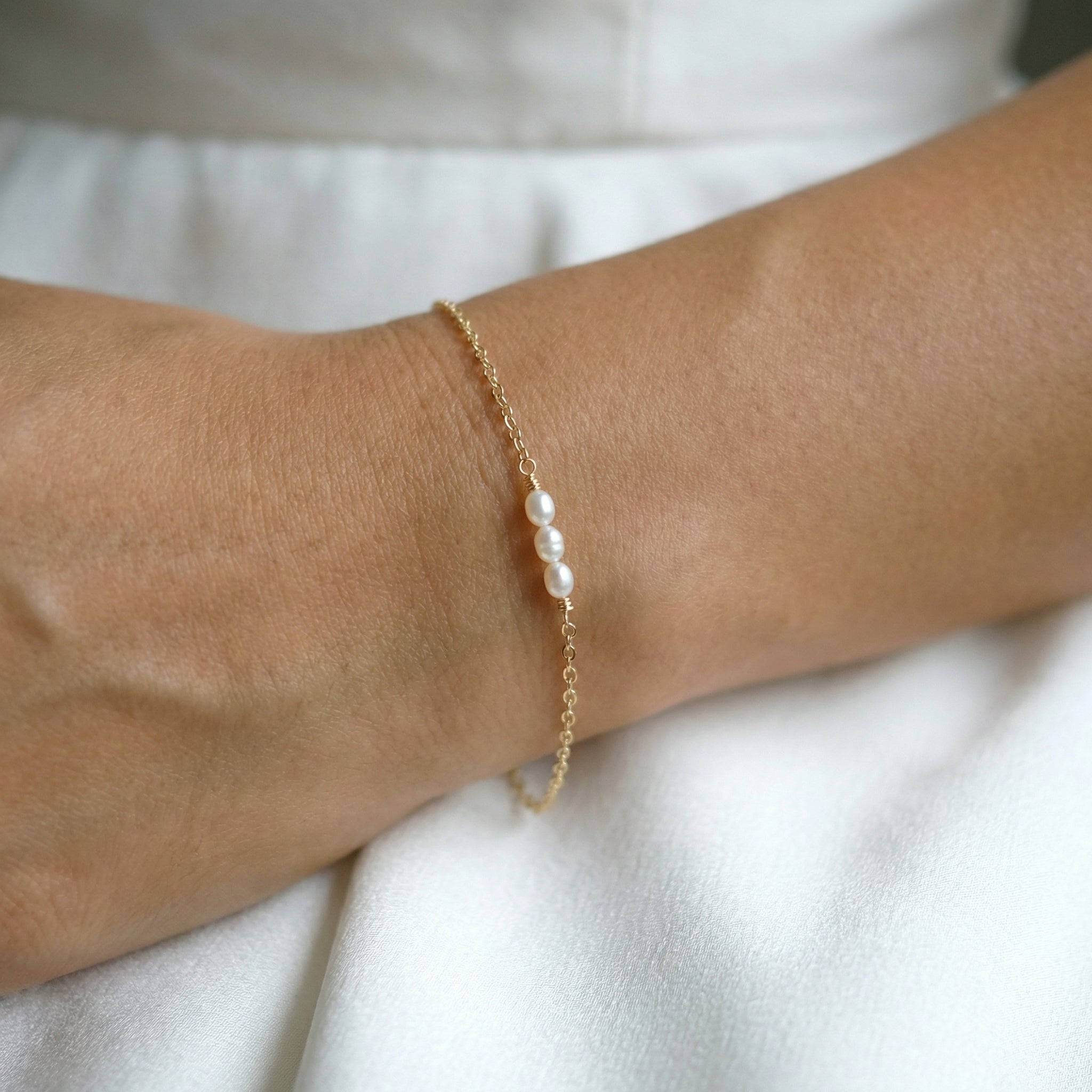 Gold bracelet with pearls on a wrist against a white background