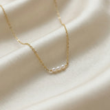 Delicate gold chain necklace with pearls on a soft beige fabric background