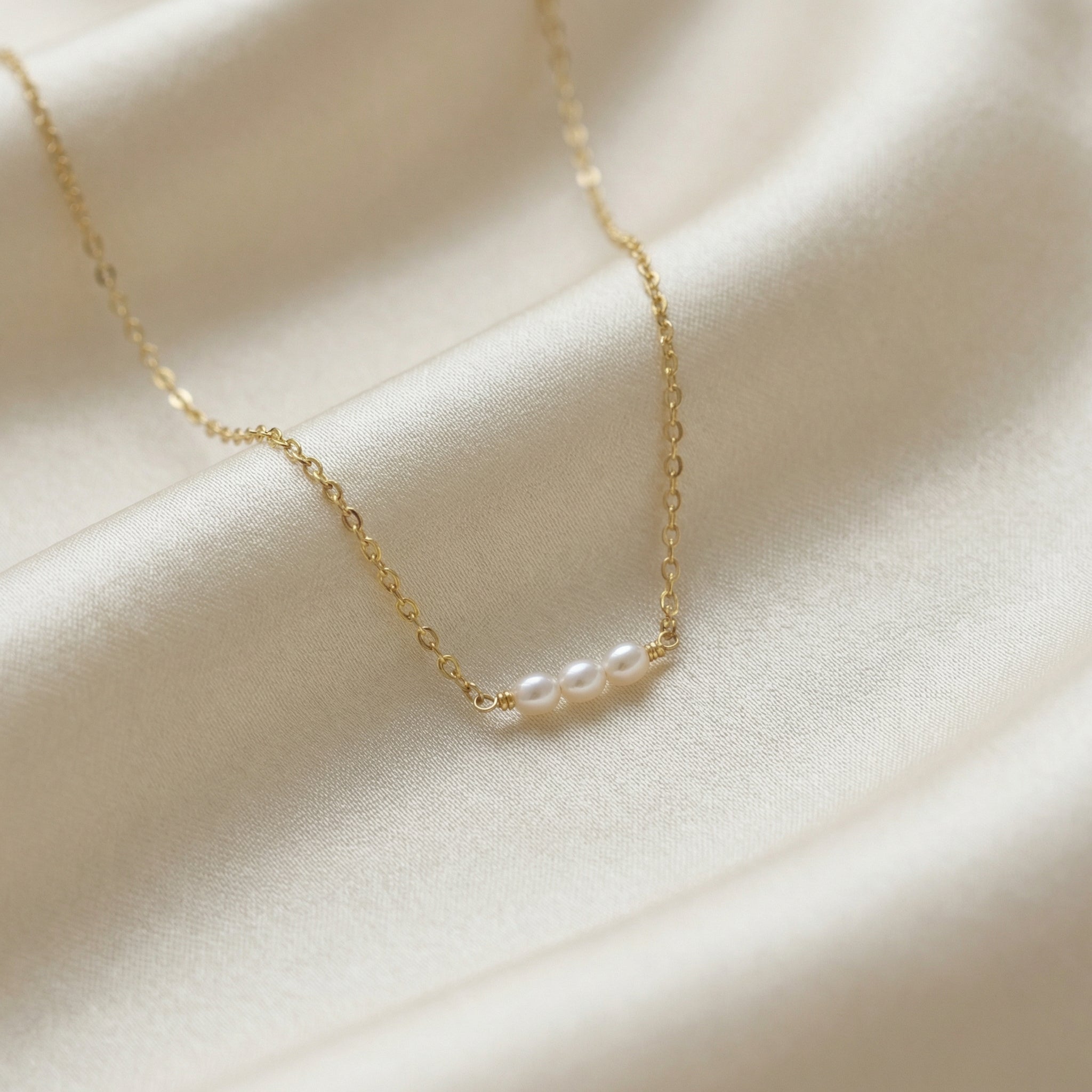 Delicate gold chain necklace with pearls on a soft beige fabric background