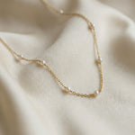 Delicate gold necklace with pearls on a beige fabric background