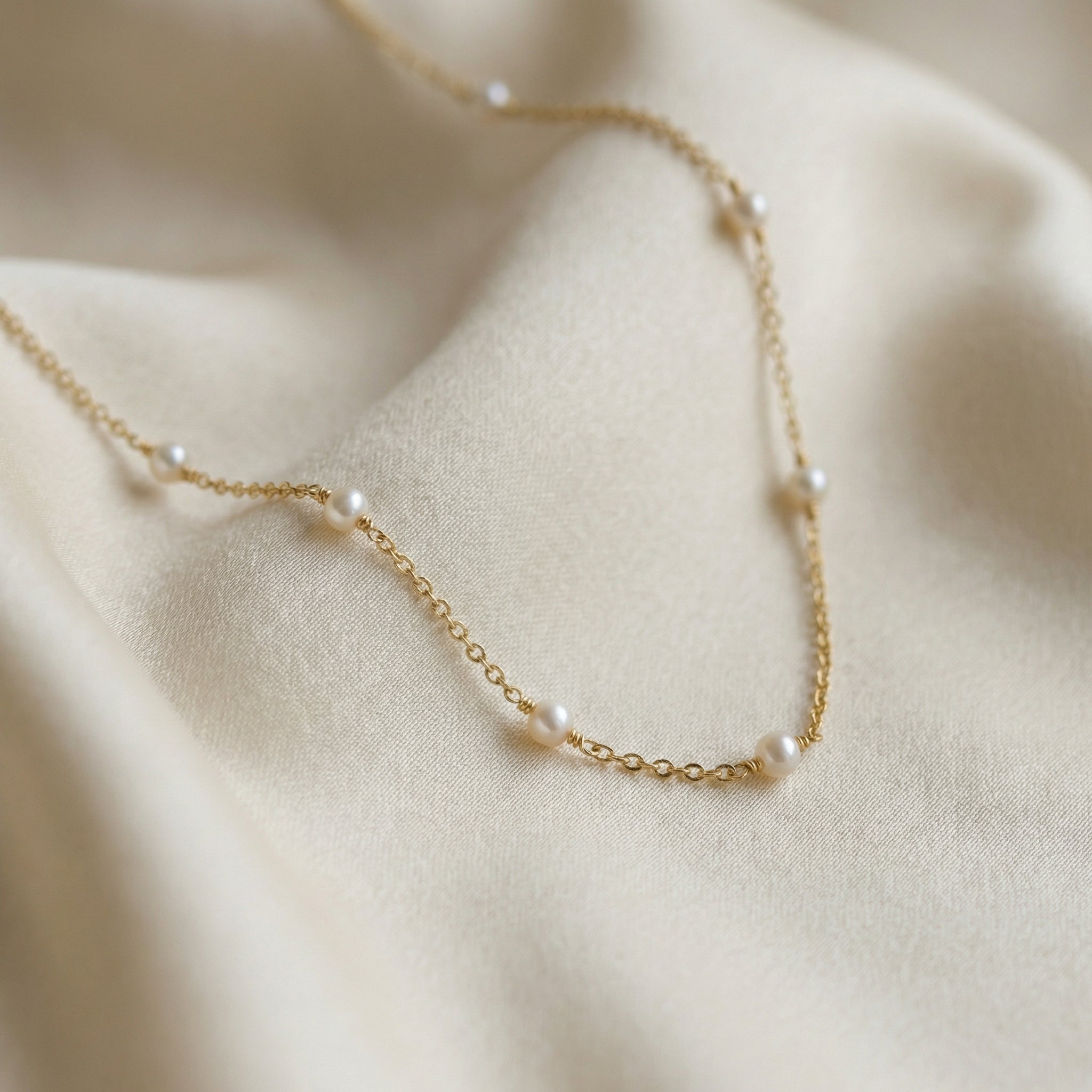 Delicate gold necklace with pearls on a beige fabric background