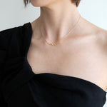 Person wearing a black one-shoulder top and gold necklace against a light background