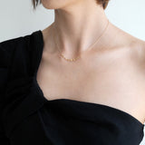 Person wearing a black one-shoulder top and gold necklace against a light background