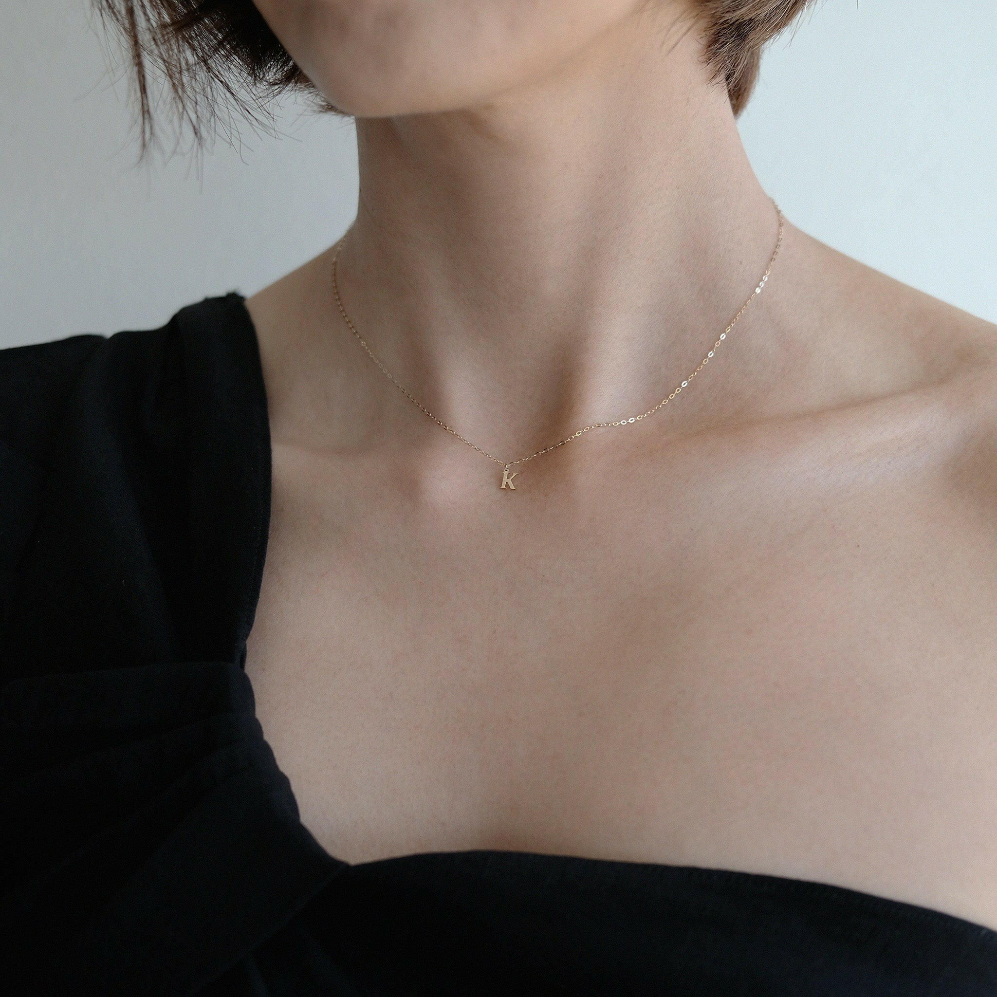Close-up of model in black off-shoulder top layering the initial necklace with subtle glow