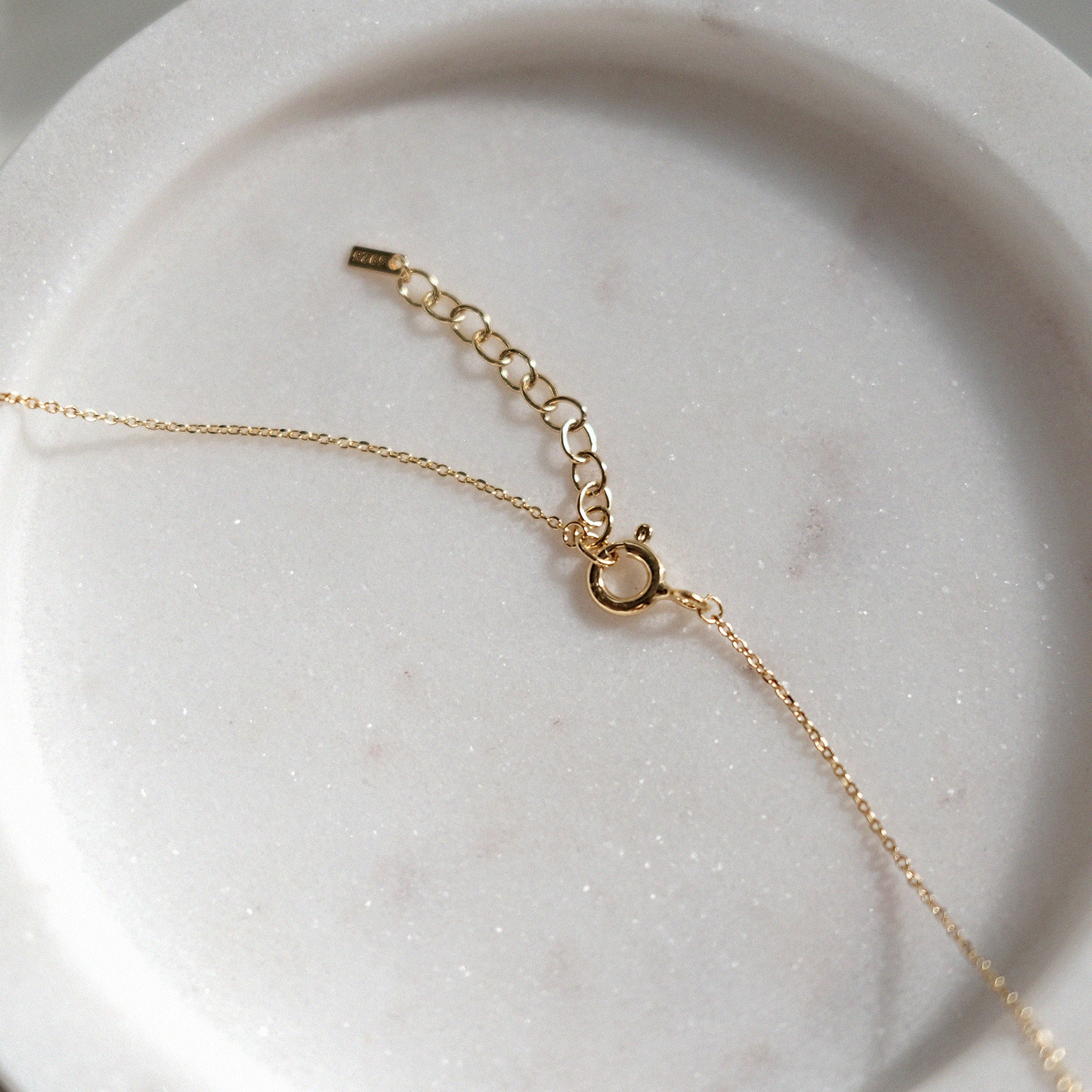 Gold necklace chain with spring ring claps and extension chain on a marble surface