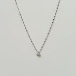Delicate twisted chain necklace with cubic zirconia centerpiece on a neutral background