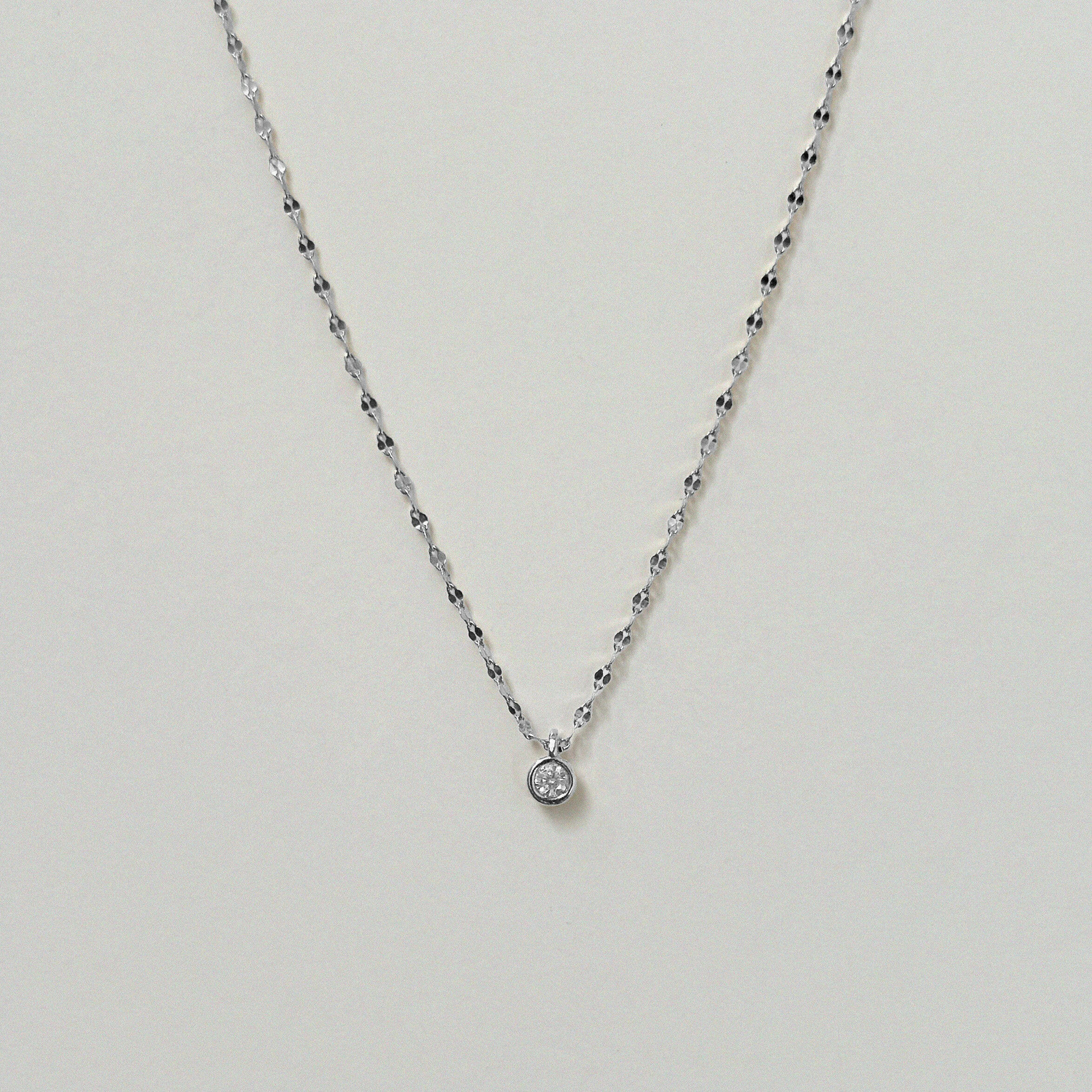 Delicate twisted chain necklace with cubic zirconia centerpiece on a neutral background