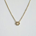 Petite 6mm gold clover pendant necklace with cubic zirconia laid flat on a light background