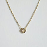 Petite 6mm gold clover pendant necklace with cubic zirconia laid flat on a light background