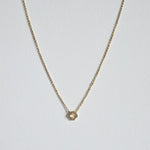 Petite 6mm gold clover pendant with dainty chain necklace laid flat on a light background