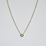Petite 6mm gold clover pendant with dainty chain necklace laid flat on a light background
